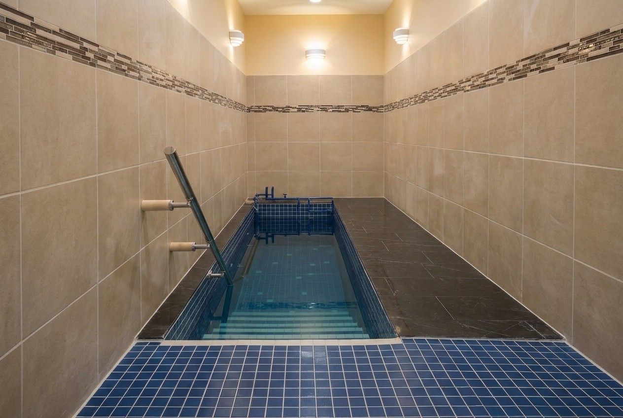 Finished mikvah with a blue-tiled pool, stainless handrail and warm wall lighting